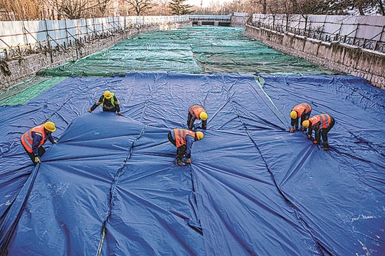 1月3日,房山区东风街道,工人正在修复的河道内给混凝土铺设保温布。